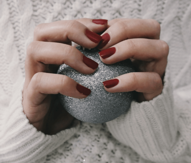 A person with red nails holding a sparkly Christmas ornament