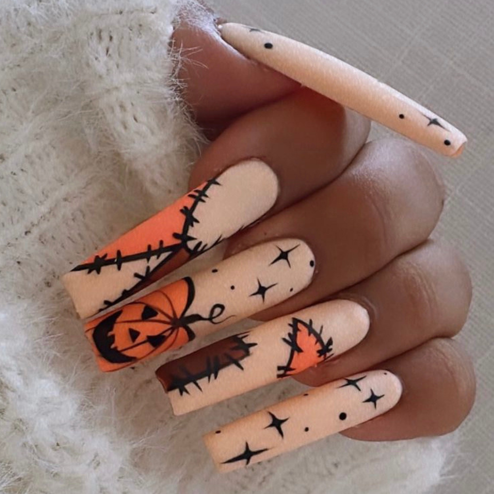 Halloween nail designs: Long square nails with a tan background. A design with stars, brown and orange patches, and a pumpkin